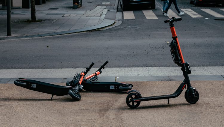 Two e-scooters on a pavement, one stood up and one lying on its side.