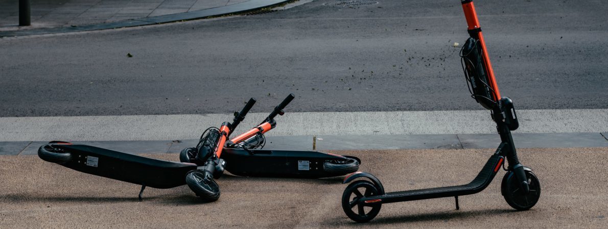 Two e-scooters on a pavement, one stood up and one lying on its side