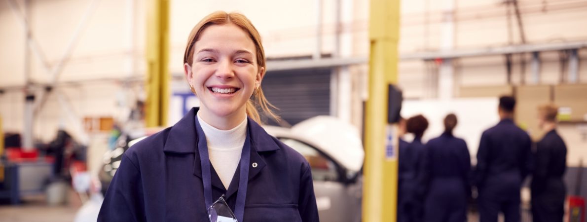 A young woman with blonde hair standing in front of a car and smiling at the camera,