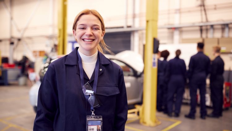 A young woman with blonde hair standing in front of a car and smiling at the camera,