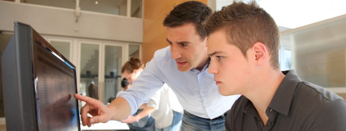 A man showing a younger man something on a computer's screen