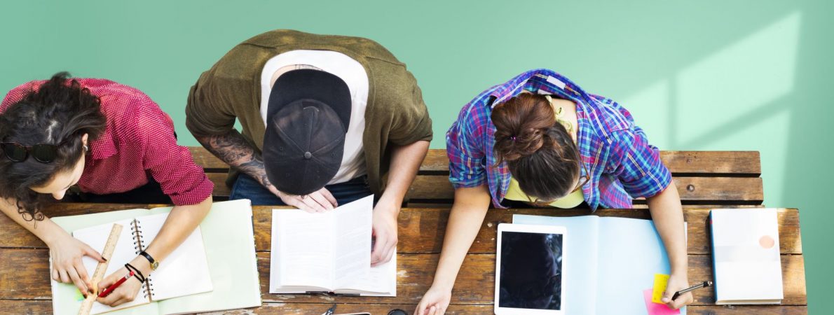 A picture taken from above that shows three young people sitting on a desk and studying