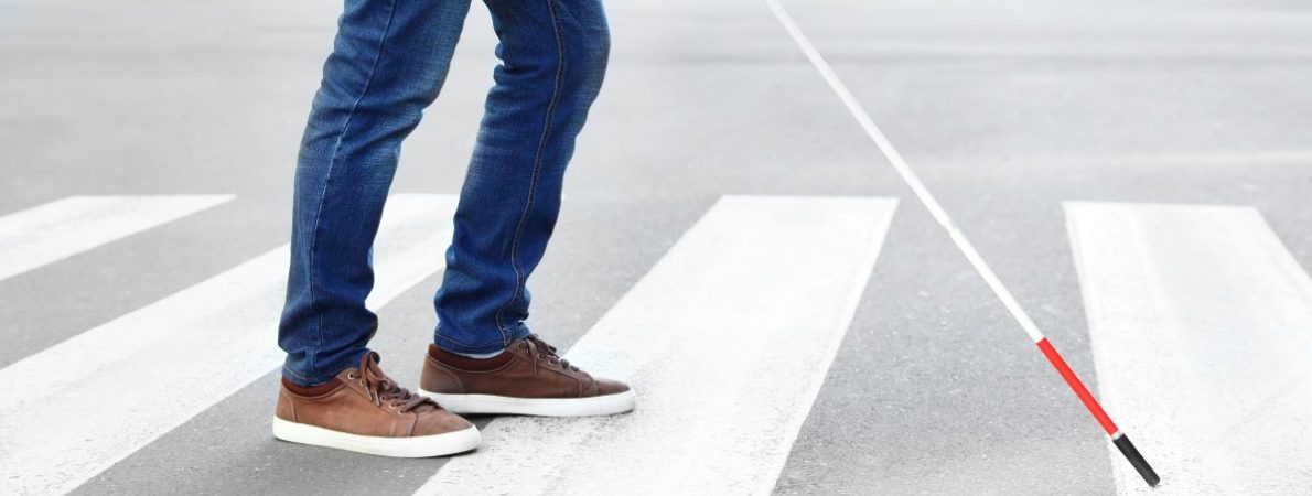 A blind person holding a cane crossing the road