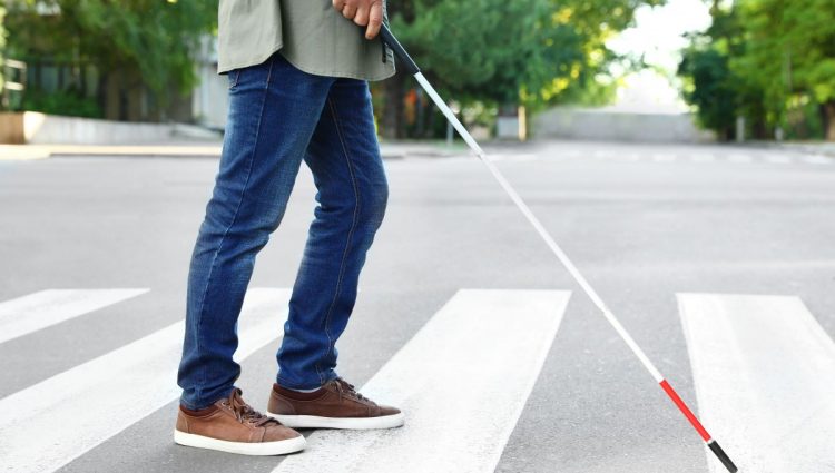 A blind person holding a cane crossing the road