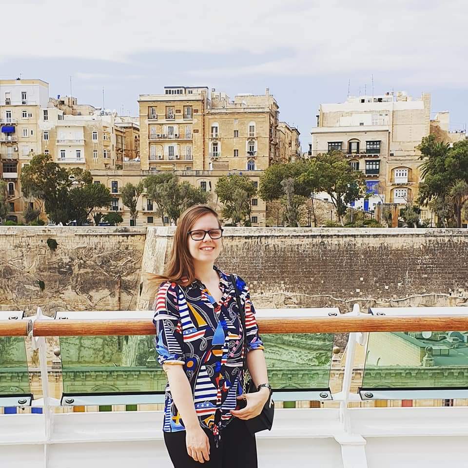 A picture of Fiona standing, looking at the camera and smiling, in front of some buildings during her holidays
