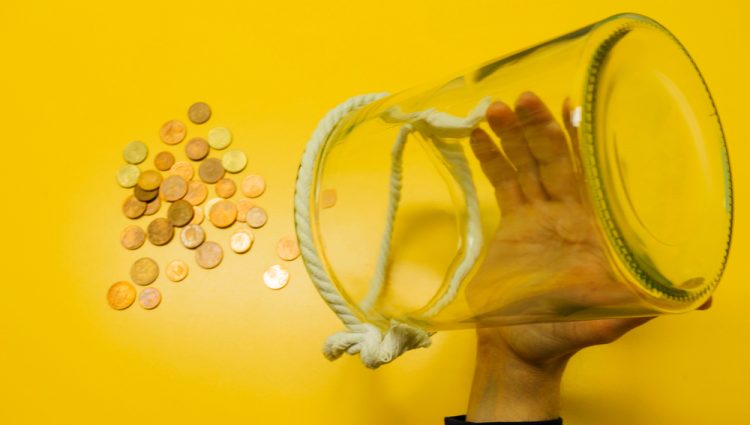 A man taking out his savings from a glass container on a table