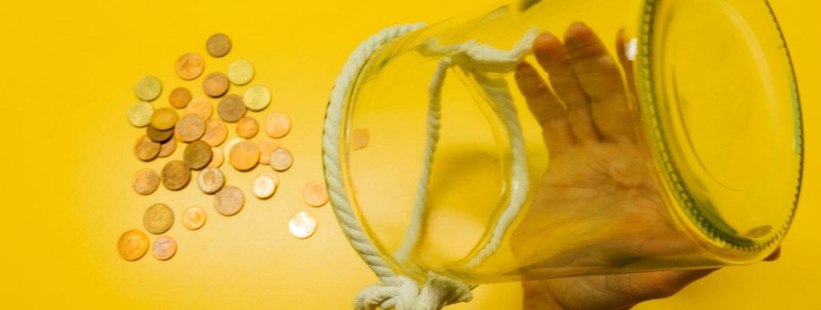 Man is taking his savings out from a glass container on a yellow table