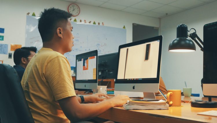 Two students working in front of Mac computers in a classroom