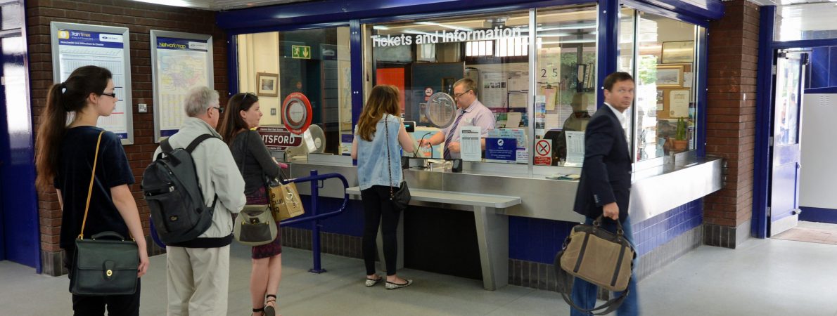A queue of people waiting at a railway station ticket office