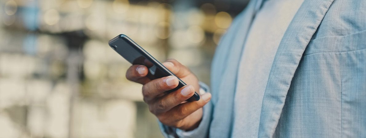 Close up picture of a man walking outside, holding a phone.