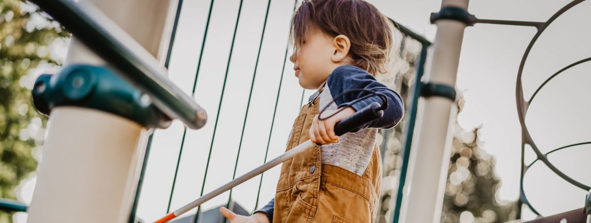 Child with white cane on play equipment