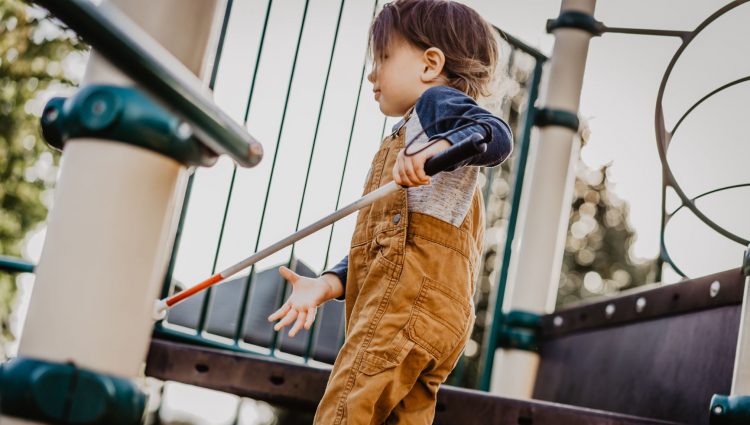 Child with white cane on play equipment