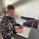 A picture showing Aleksandr studying in front of his laptop, sat on a desk in his bedroom.
