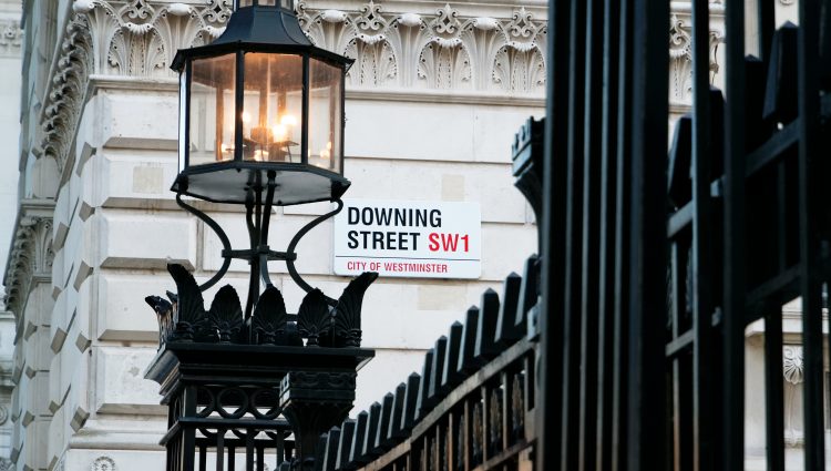 Image shows Downing Street's sign in Westminster. Downing St. road sign and building