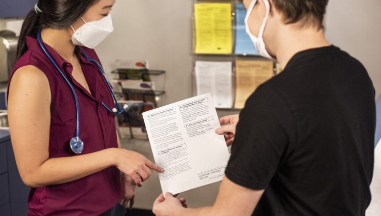 Two medical professionals consulting each other. One is holding a piece of paper and the other is pointing at it discussing.