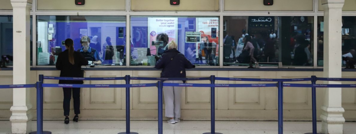 A train ticket office inside a station with two people waiting to get their tickets