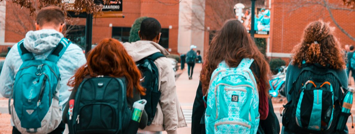 Five students walking to college with backpacks on.