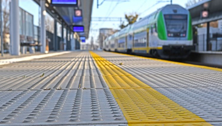 A train platform with tactile paving. A train is approaching the platform