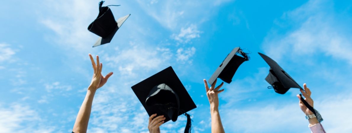 Four people throwing four graduation hats in the air.