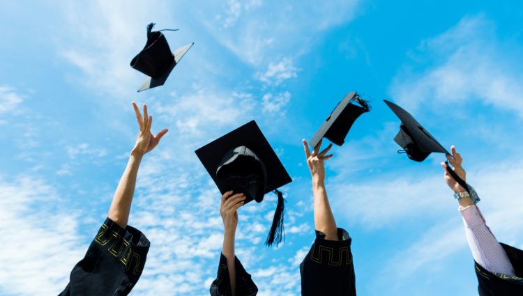 Four people throwing four graduation hats in the air.
