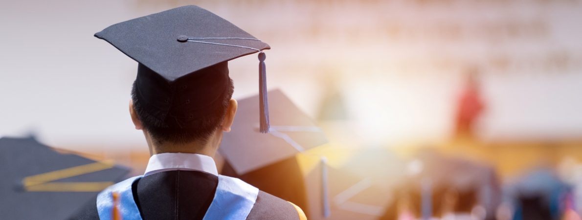 Rear view of a graduation ceremony. A man is wearing a graduation hat and a gown.