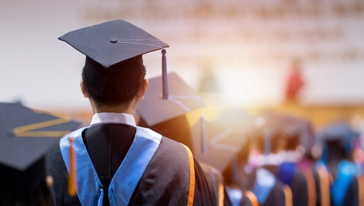 Rear view of a graduation ceremony. A man is wearing a graduation hat and a gown.