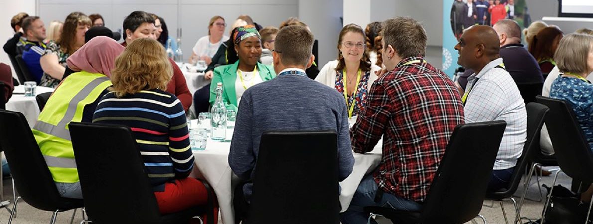 Sight Loss Councils' volunteers sat around table in a reception room. In the background is a Sight Loss Councils banner.