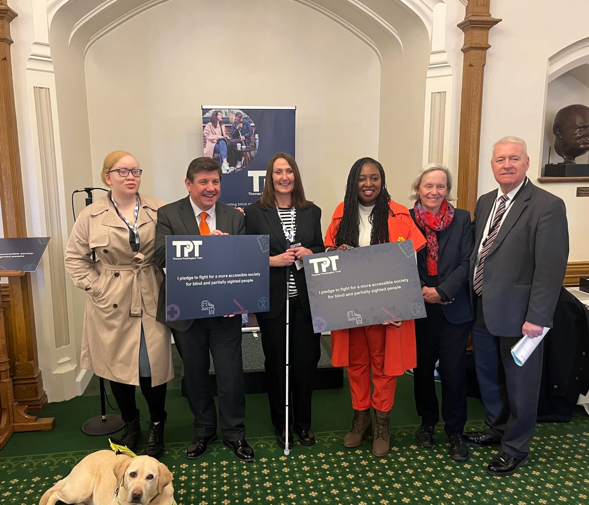 Image shows TPT staff and MPs in a group photo with MPs holding our pledge boards. A TPT banner is in the back, as well as a guide dog lying on the floor, in the bottom left.