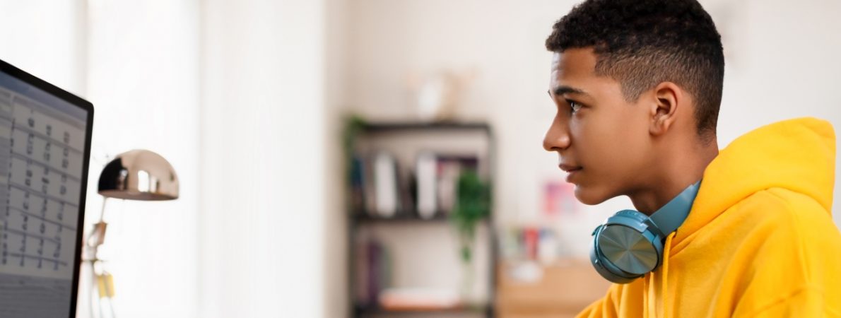 A young adult engages with work on a large screen desktop computer at a desk.