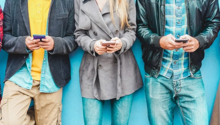 A group of students using mobile smart[hones, standing in a row.
