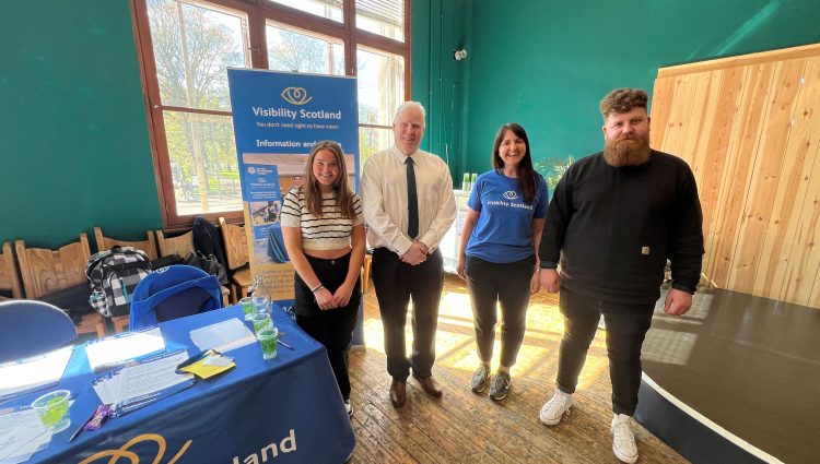 Photo taken at the launch event of Sight Loss Councils Scotland. From left to right: Lara, SLC volunteer, Iain Mitchell, Senior Engagement Manager for Sight Loss Councils North, Emma Scott, Head of Operations, Visibility Scotland, and Callum Lancashire, Engagement Manager for Sight Loss Councils Scotland. They are stood together next to a Visibility Scotland banner, smiling at the camera.