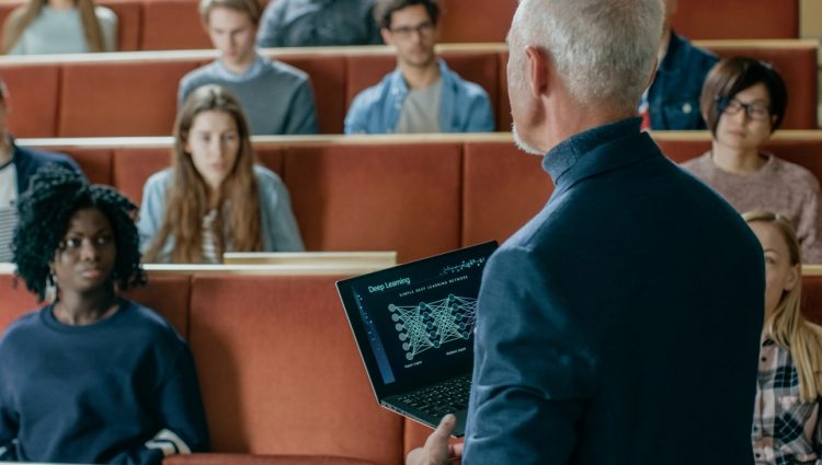 Professor of Computer Science Reads Lecture from a laptop to a Classroom Full of Multi Ethnic Students.