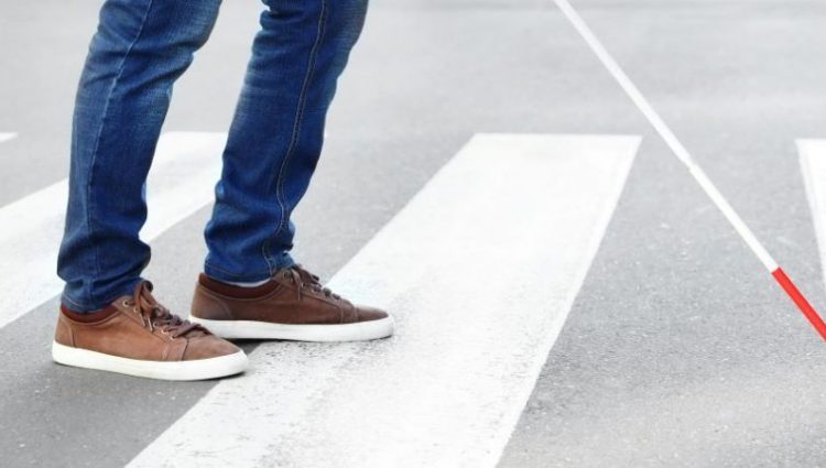 A blind person holding a cane crossing the road