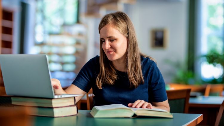 A visually impaired woman sitting and studying in the university library using laptop and books