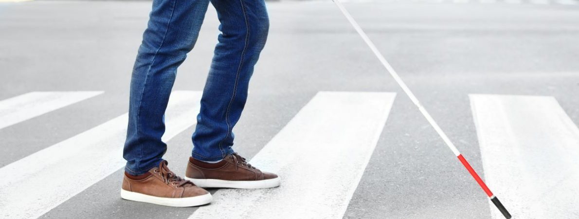 A blind person holding a cane crossing the road.
