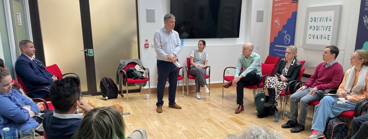 Image shows Channel 4 skill share session taking place at the TPT hub. A man is stood in a meeting room, talking to a group of people sat in a semi-circle formation in front of him.