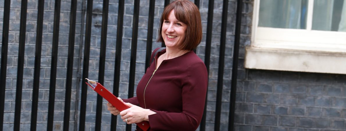 Photo shows Chancellor Rachel Reeves walking and smiling holding her red ministerial folder
