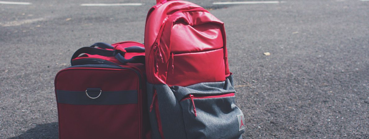 A picture of a small red suitcase and red and grey rucksack on a road.