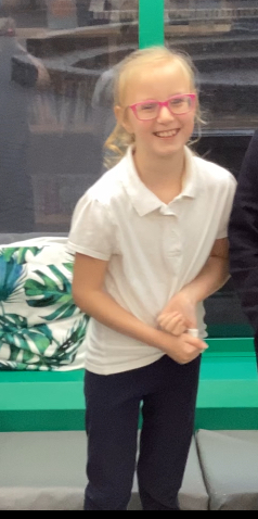 A student in a white polo shirt stands in front of of a green and grey background, ready and excited to play some sports.