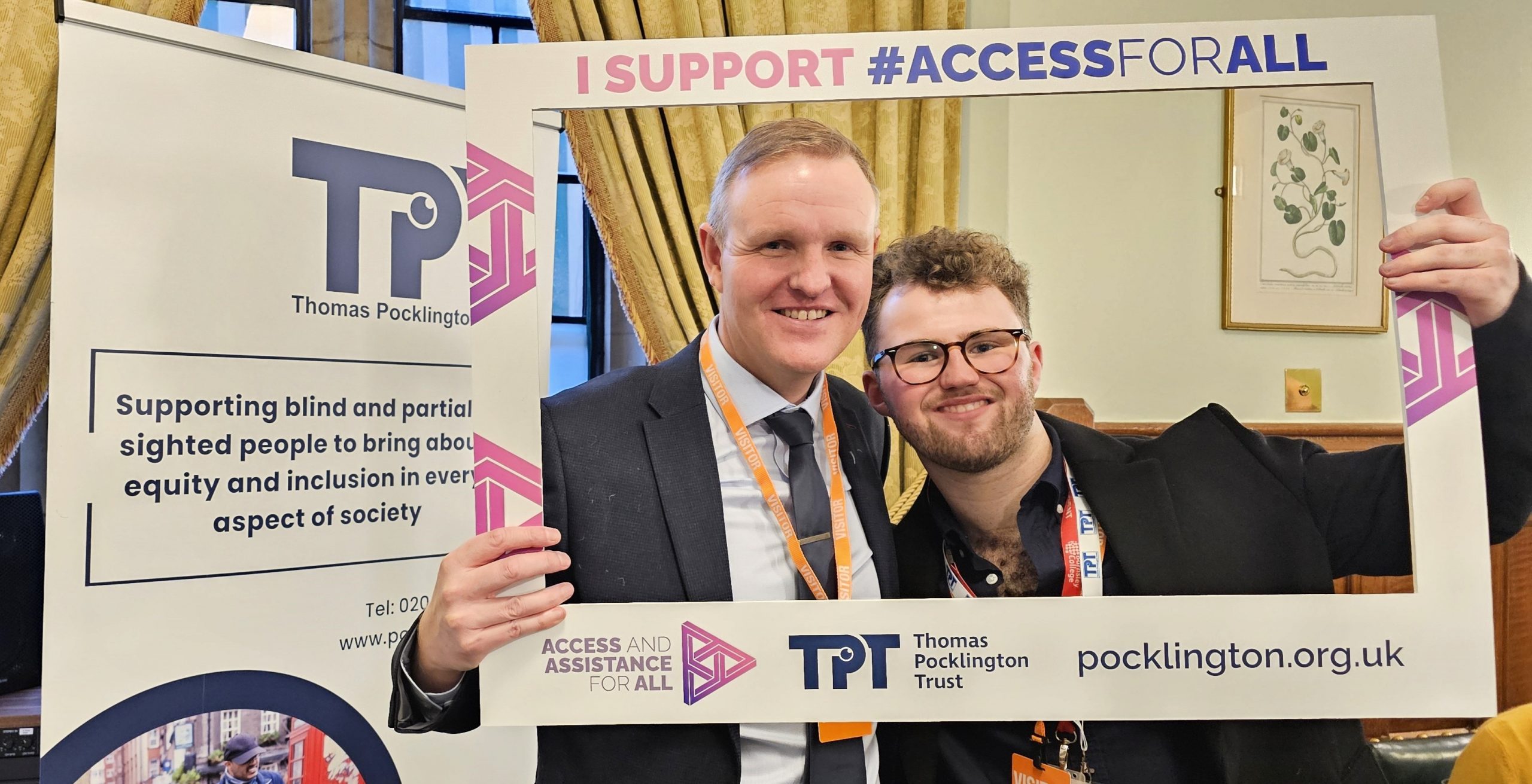 Tom and Gavin Batty are are smiling and holding a large frame that reads I SUPPORT #ACCESSFORALL, dressed smartly. 