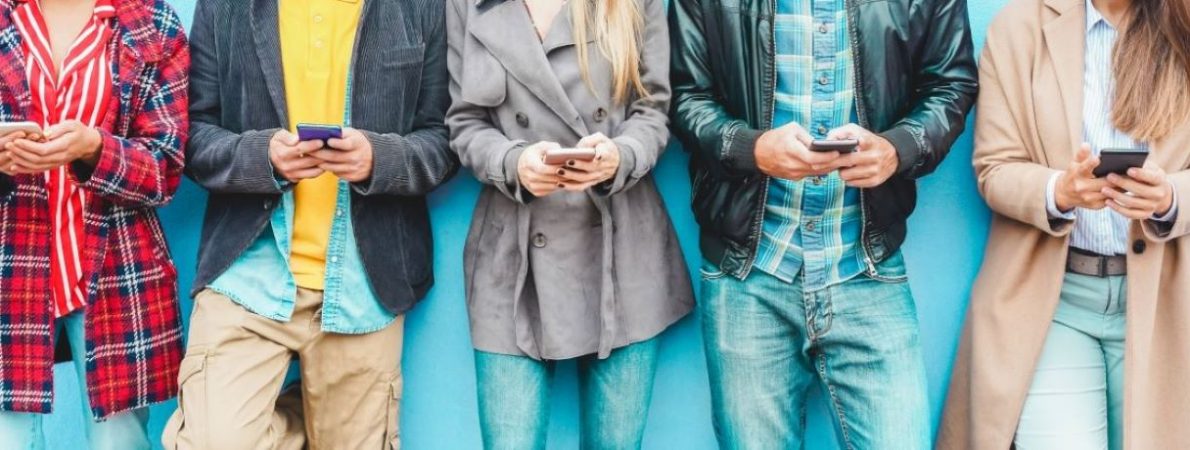 A group of students using mobile smart[hones, standing in a row.