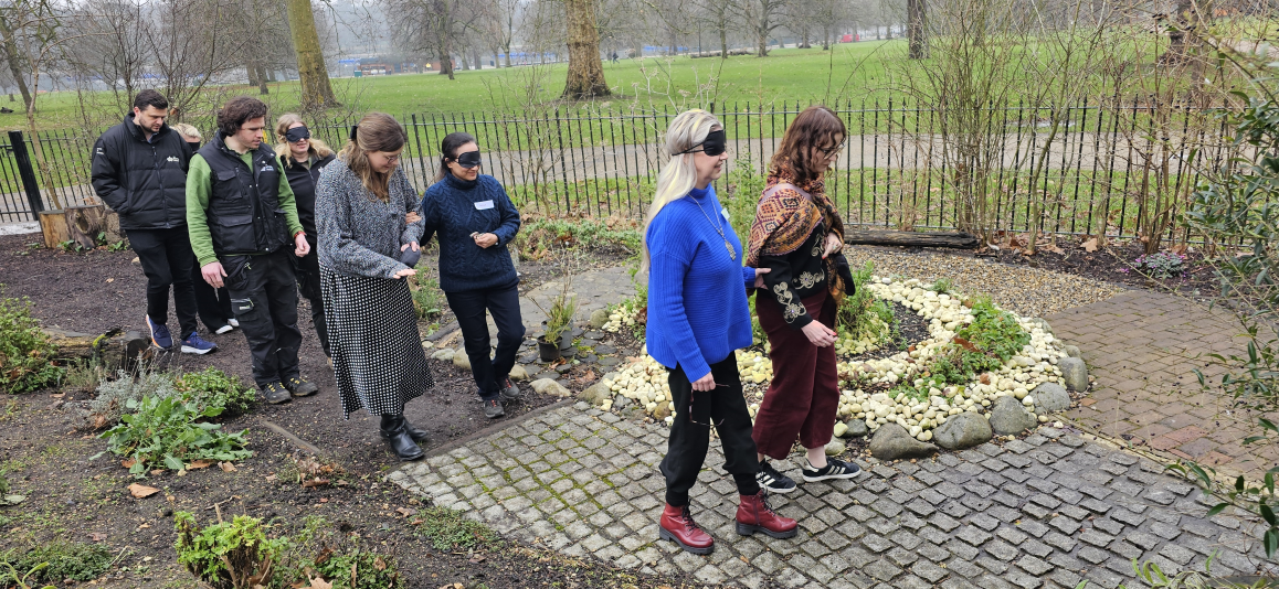 A wintery day, where two people with eye covers are leading a group of people behind them through a landscaped courtyard area within one of the Royal Parks