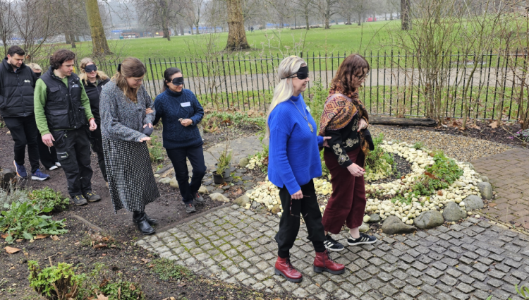 A wintery day, where two people with eye covers are leading a group of people behind them through a landscaped courtyard area within one of the Royal Parks