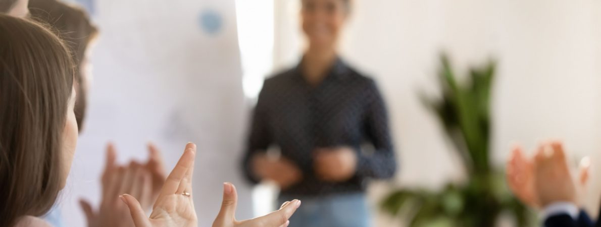 A close up of people applauding a speaker who is blurred in the background.