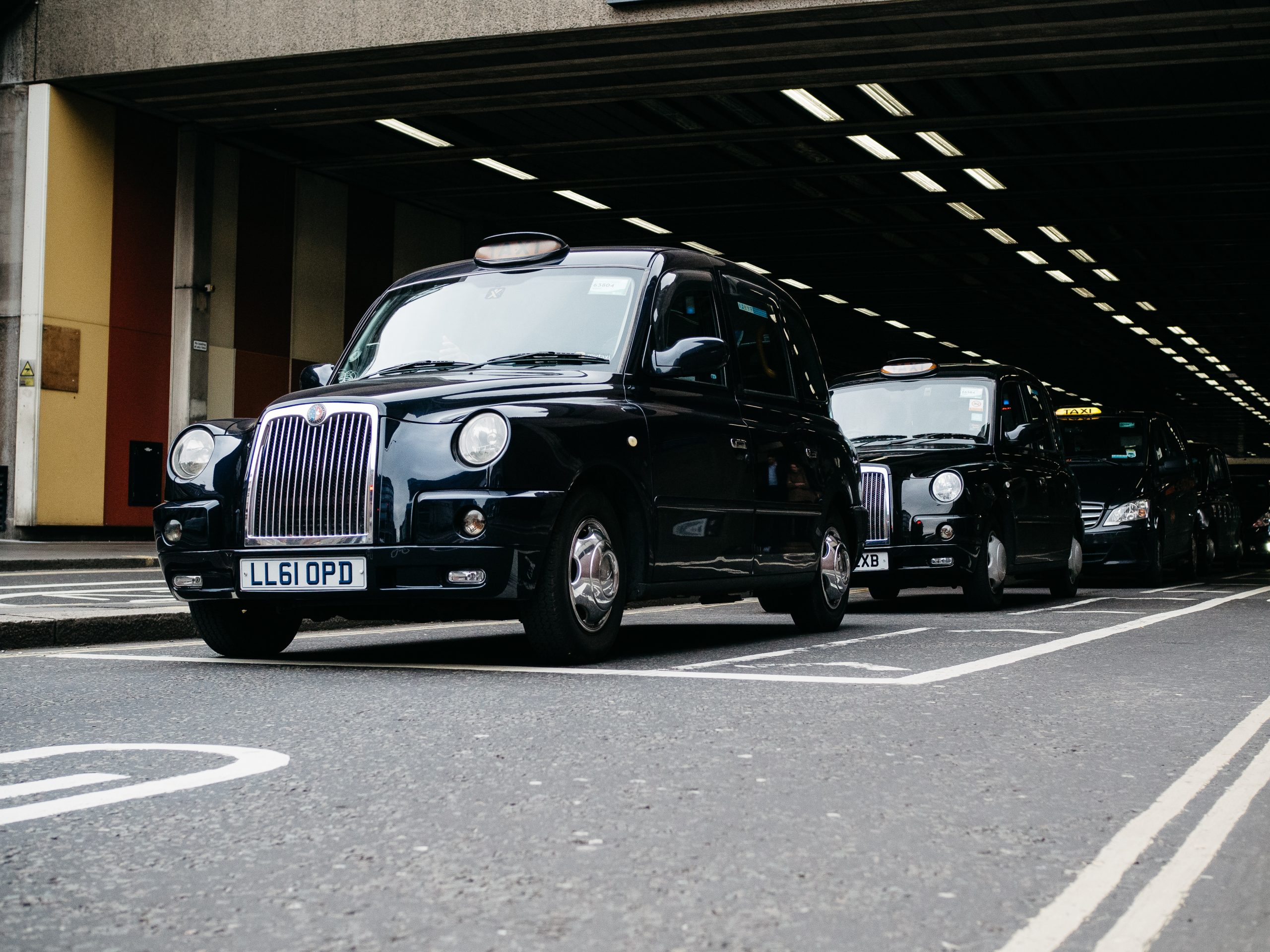Two black taxis are lined up in a tunnel or underpass, one in front of the other.