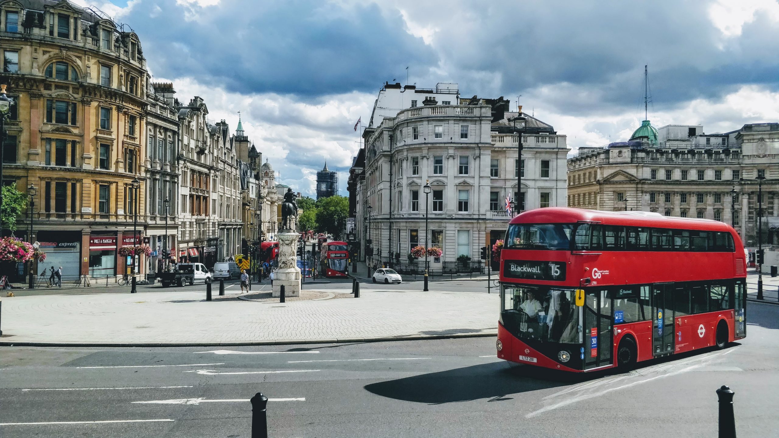 A red London bus driving through the city centre, past tall office buildings.