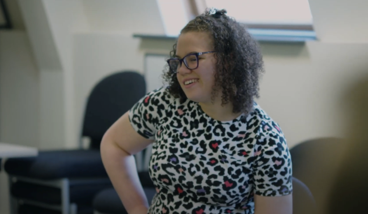 Samiya is wearing a black and white leopard print top, smiling while looking to her left