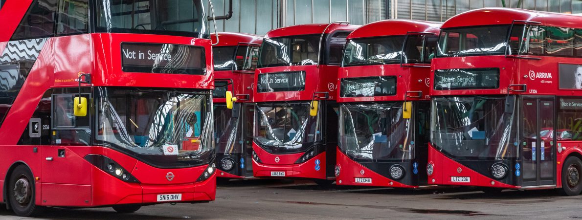 Four red London buses stood in a bus garage