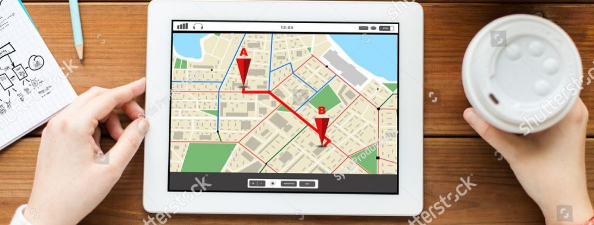 A student is using a tablet showing a map application, planning a journey with a cup of coffee to the right hand side.