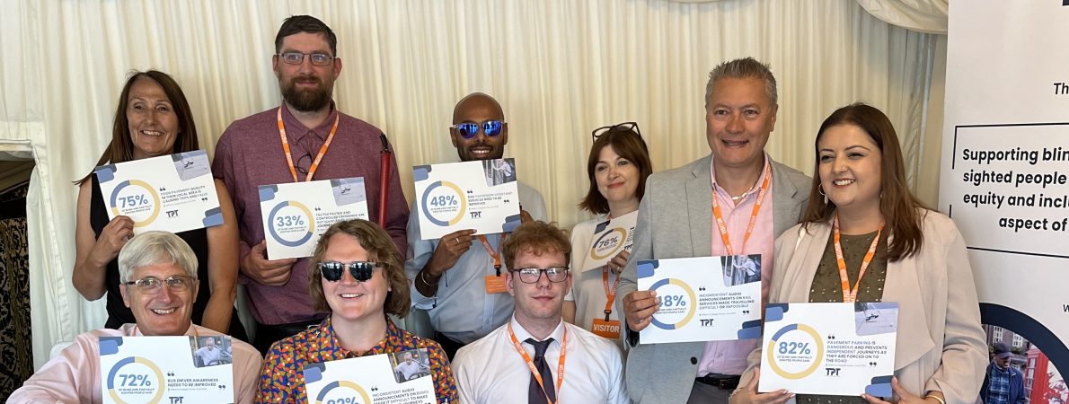9 TPT staff with lived experience of sight loss in two rows hold up boards which show in large letters different statistics relating to sight loss. The back are standing whilst the front row are seated.